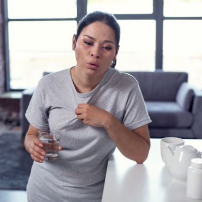 Woman leaning on bench holding glass of water looking hot and distressed. Adobe.